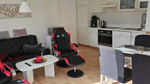 Ein modernes Wohnzimmer mit einem schwarz-roten Sofa, einem kleinen weißen Couchtisch und einem Essbereich mit Tisch und Stühlen.