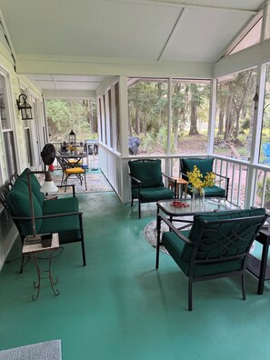 A covered porch with green chairs, a table, and a fan.