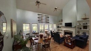 A spacious living room with a dining area, large windows, a fireplace, and a TV. - Single Family Home, Land trans Round Trip! Melrose Pool Open! (Daufuskie Island)