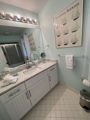 A bathroom with a sink, mirror, and a poster of sailboats.