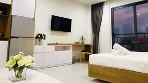 Une chambre d’hôtel moderne équipée d’un lit, d’une télévision, d’un bureau et d’une petite table sur laquelle est posé un vase de fleurs.