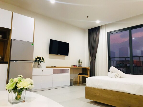 Ett modernt hotellrum med en säng, en tv, ett skrivbord och ett litet bord med en vas med blommor.