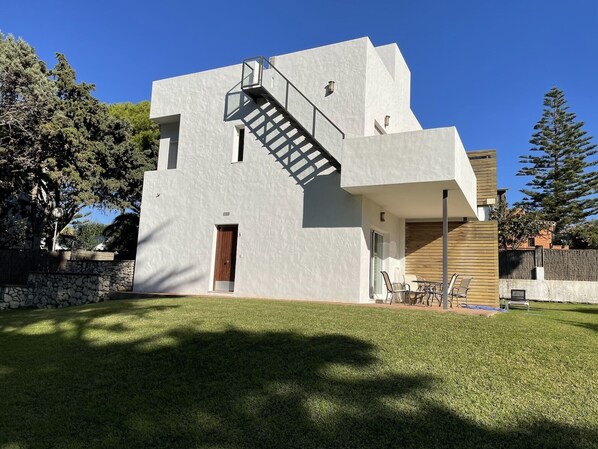 Uma casa moderna com escada que leva ao andar superior, uma pequena porta e área de varanda com mobiliário de exterior.