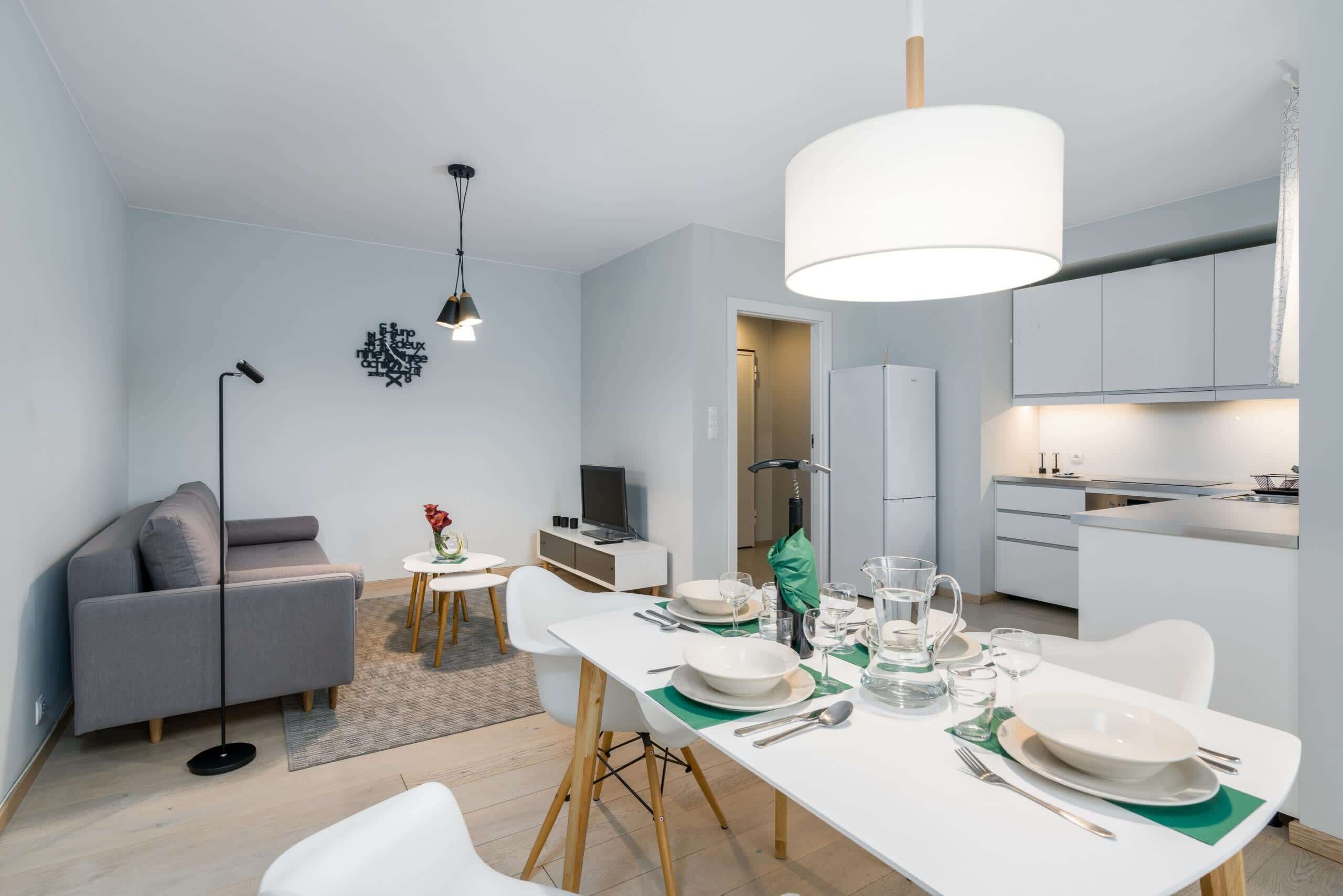 A modern apartment with a dining area, kitchenette, and a grey sofa.