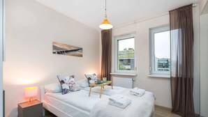 Ein modernes Schlafzimmer mit Bett, Nachttisch, Lampe und einem Fenster mit Vorhängen.