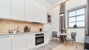 Eine moderne Küche mit weißen Schränken, einem Einbauofen und einer Essecke mit zwei Stühlen und einem Tisch.