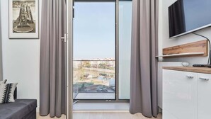 Ein modernes Zimmer mit einer Schiebeglasdoor zu einem Balkon, einem an der Wand montierten Flachbildfernseher und einer schlichten Küchenzeile.