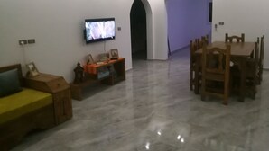 A modern living room with a flat-screen TV mounted on the wall, a wooden dining table with chairs, and a sofa. - Superb villa near the sea (Houmt Souk)