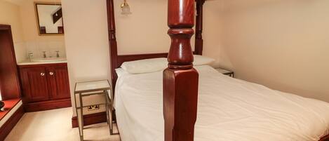 A four-poster bed with white linens, a wooden nightstand, a small table, and a mirror above the sink in a hotel room.