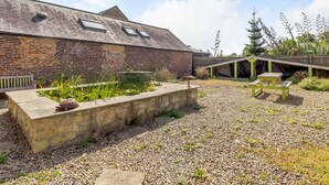 A rustic barn with a gravel courtyard, a wooden bench, and a raised garden bed. - The Granary (Morpeth)