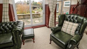 A room with a large sliding glass door leading to a garden, two leather armchairs with matching cushions, and a wooden staircase in the background. - The Granary (Morpeth)
