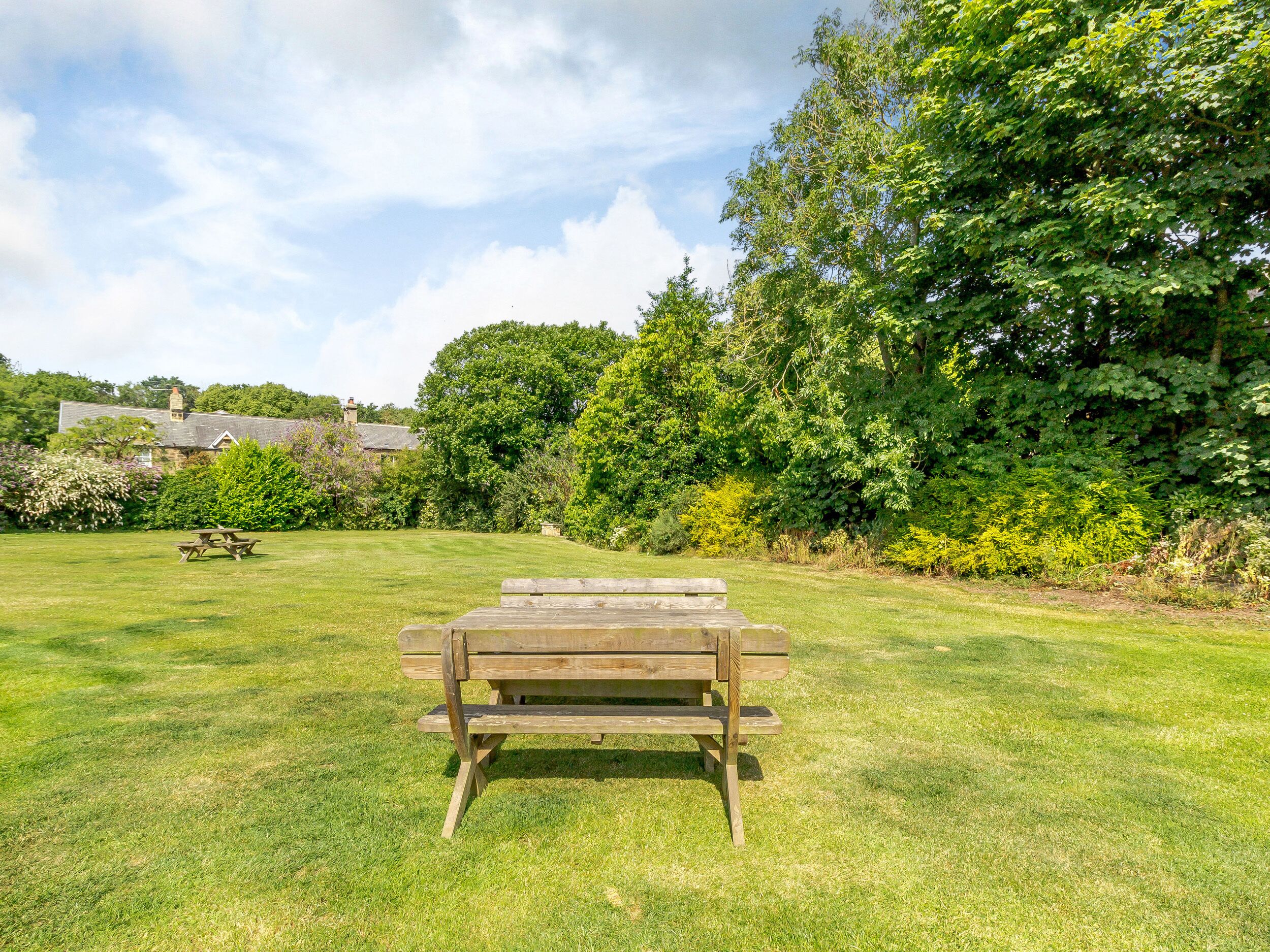 A wooden picnic table in a grassy area with a house in the background.