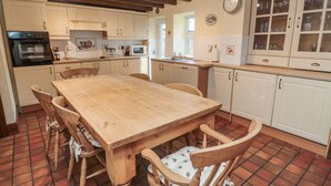 A kitchen with a wooden table and chairs, white cabinets, and a tiled floor. - The Granary (Morpeth)