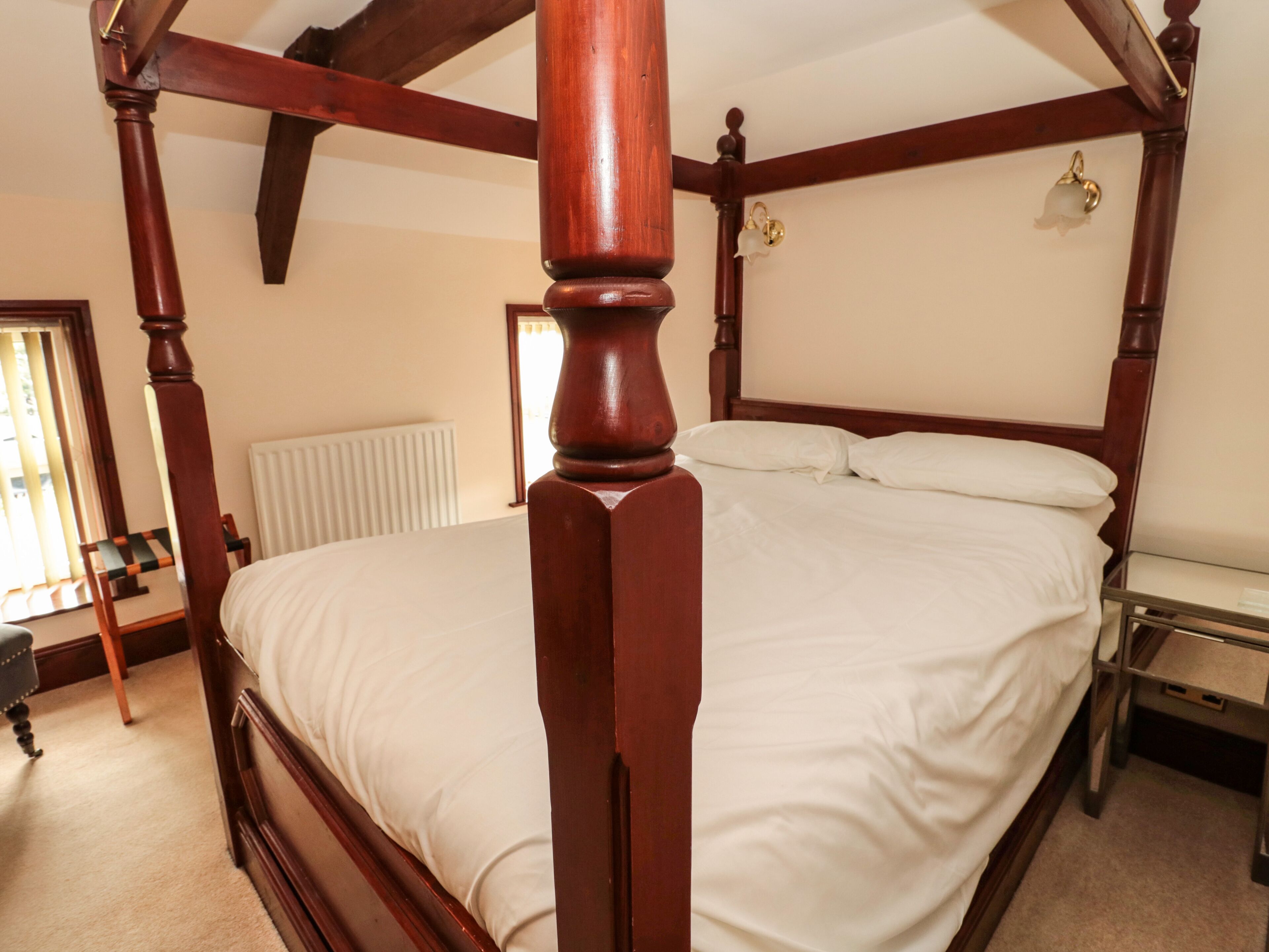 Een kamer met een bed met hemelbed, houten frame en witte beddengoed, evenals een radiator en een stoel.