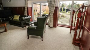 A living room with a leather sofa, a green armchair, and a wooden staircase. - The Granary (Morpeth)