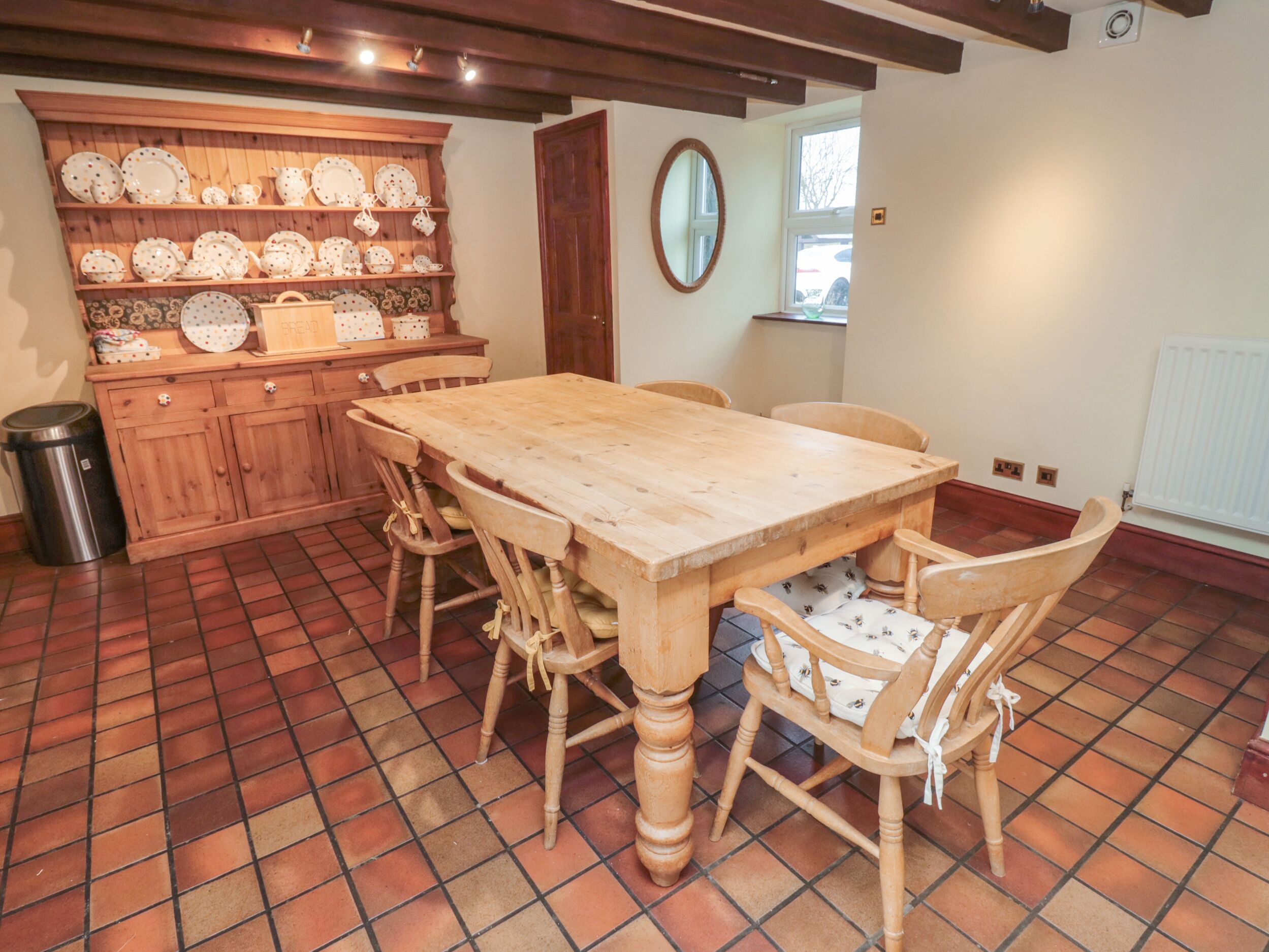 Un comedor con una mesa y sillas de madera, un armario de madera con vajilla y un suelo de baldosas.