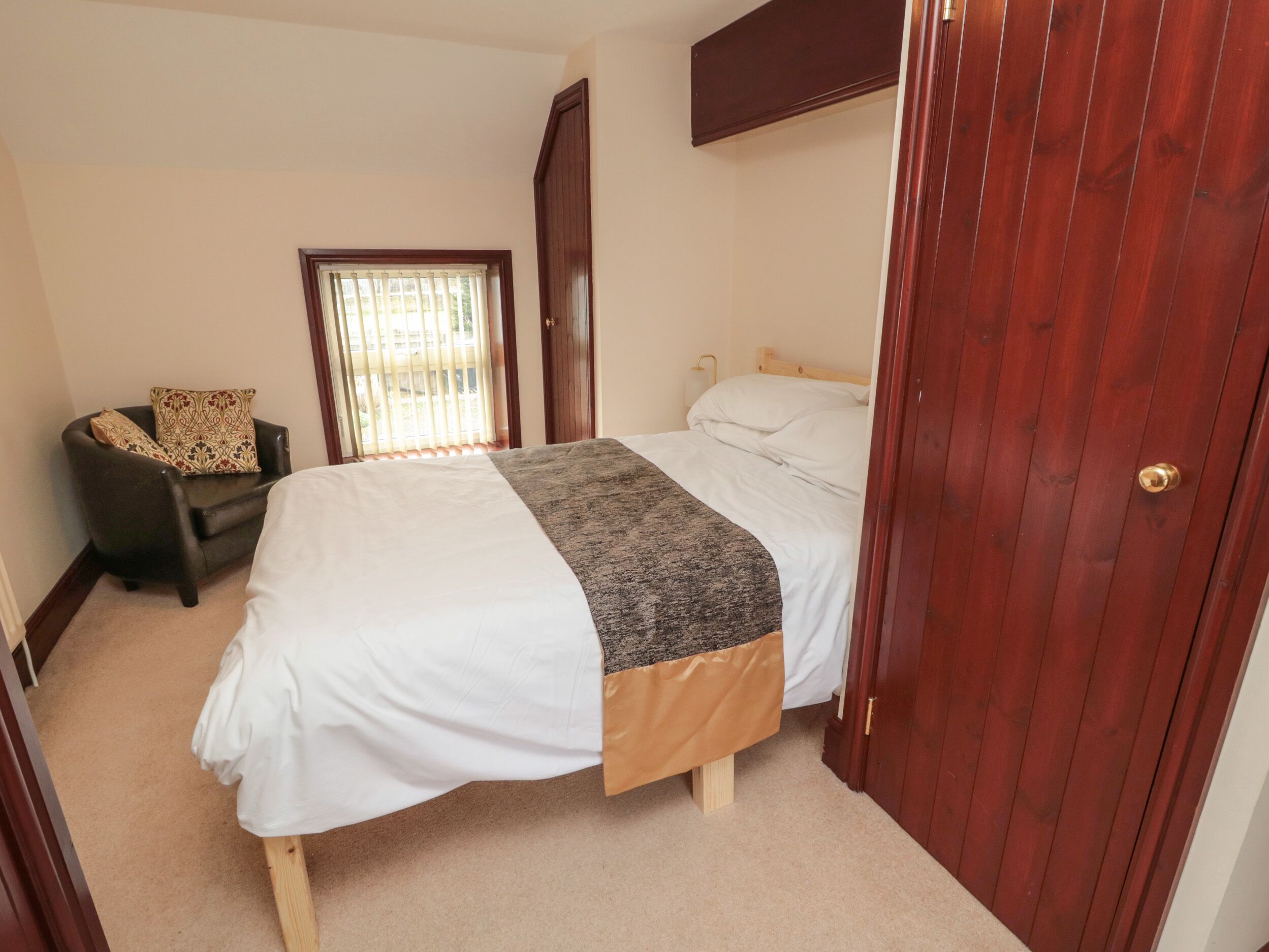 Een slaapkamer met een bed, een stoel, een deur en een raam met zonwering.
