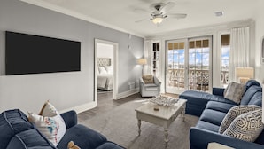 A living room with a blue sofa, a coffee table, and a ceiling fan. - The Village 3BR | Pool • Shops • Dining • Beach (Seacrest Beach)