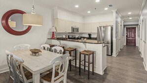 A modern kitchen with white cabinetry, a stainless steel refrigerator, and a dining area with a white table and chairs. - The Village 3BR | Pool • Shops • Dining • Beach (Seacrest Beach)