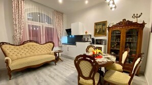 Un comedor con una mesa redonda y cuatro sillas, un sofá, un armario y un ventanal con cortinas.