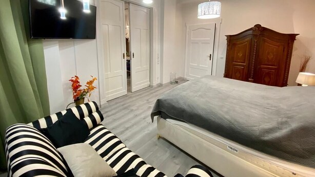 Un dormitorio con cama, televisor montado en la pared, armario de madera y cortina verde.