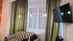 Una sala de estar con un sofá a rayas, un televisor montado en la pared y una ventana con cortinas.