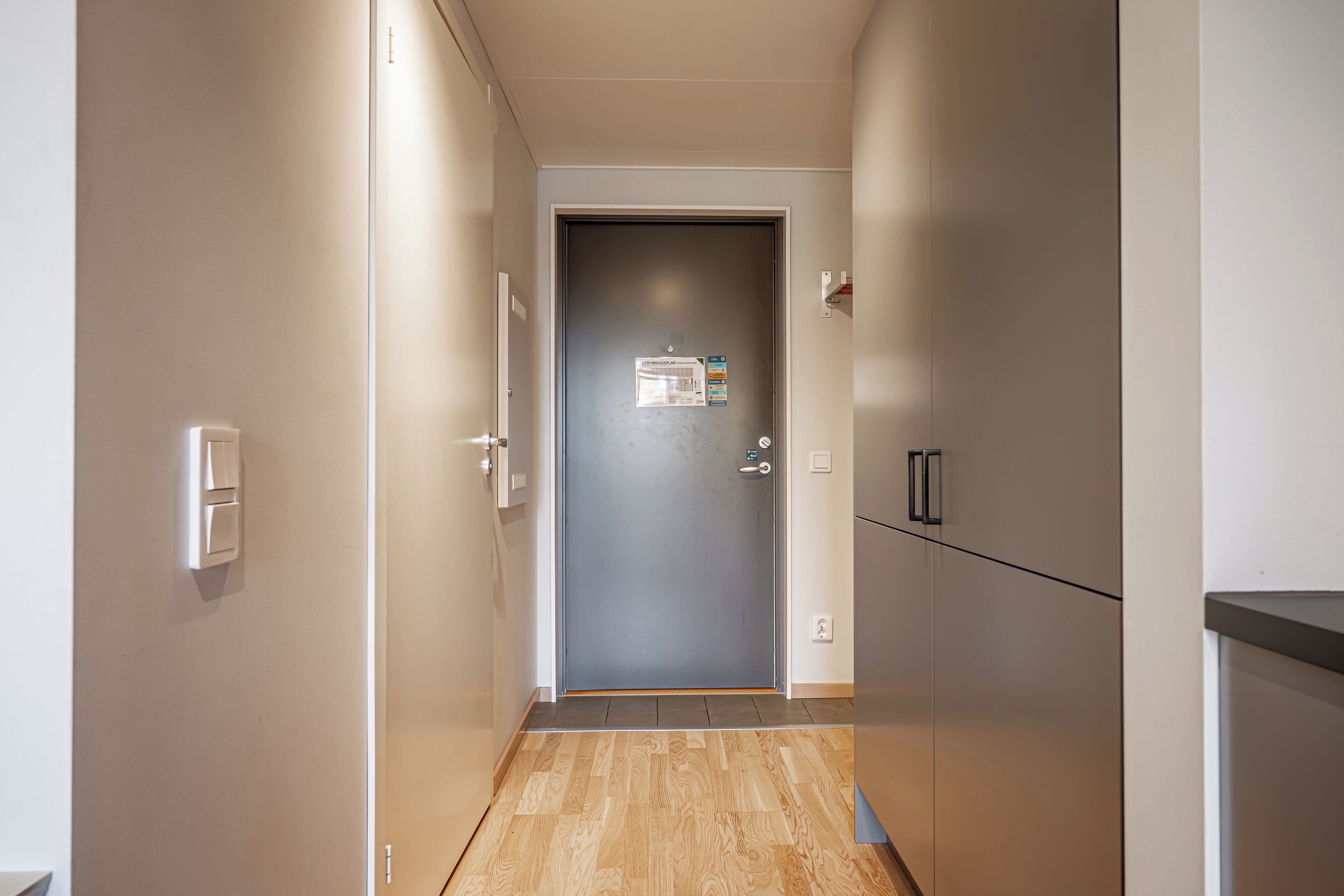 A narrow hallway with a door at the end, a light switch on the wall, and a thermostat on the door.