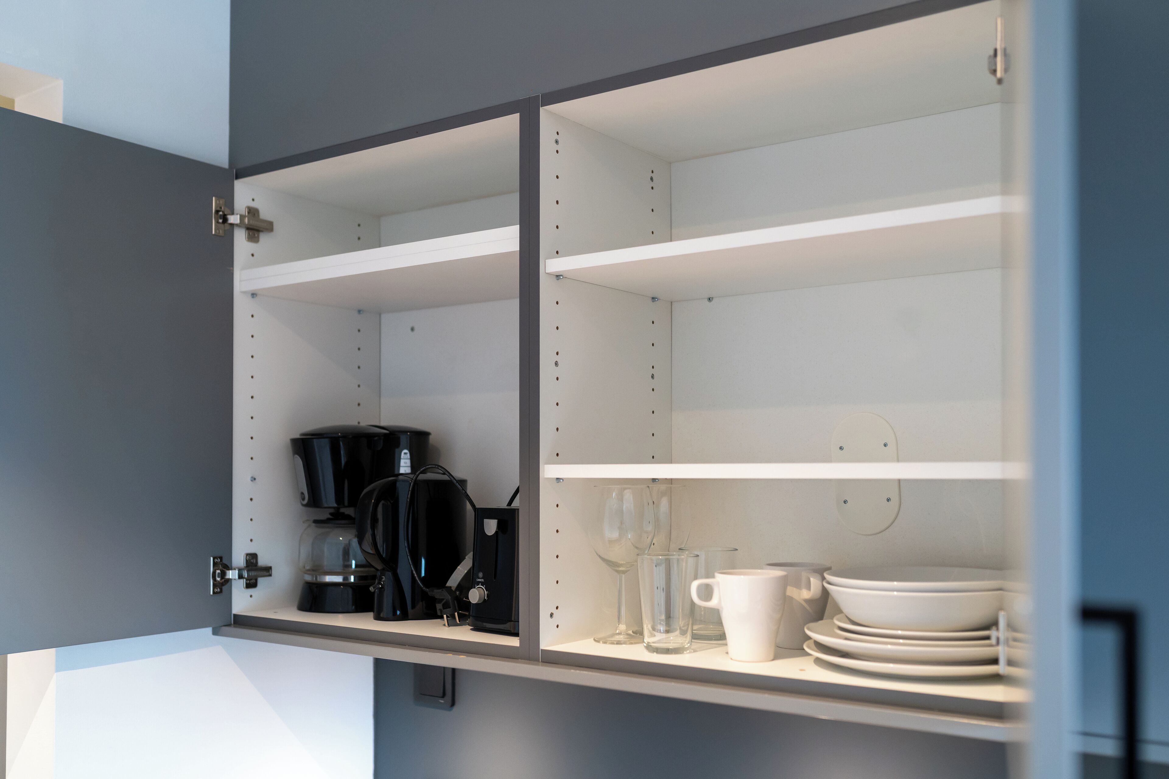 A kitchen cabinet with shelves, a coffee maker, and glassware.
