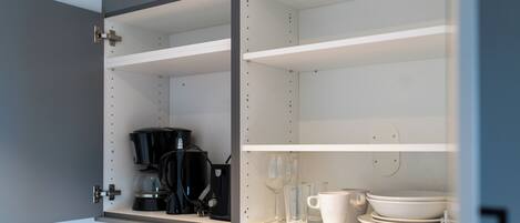 A kitchen cabinet with shelves, a coffee maker, and glassware.