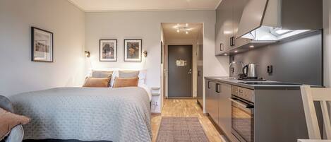 Una habitación de hotel moderna con cama, mesita de noche, lámpara y una zona de kitchenette.