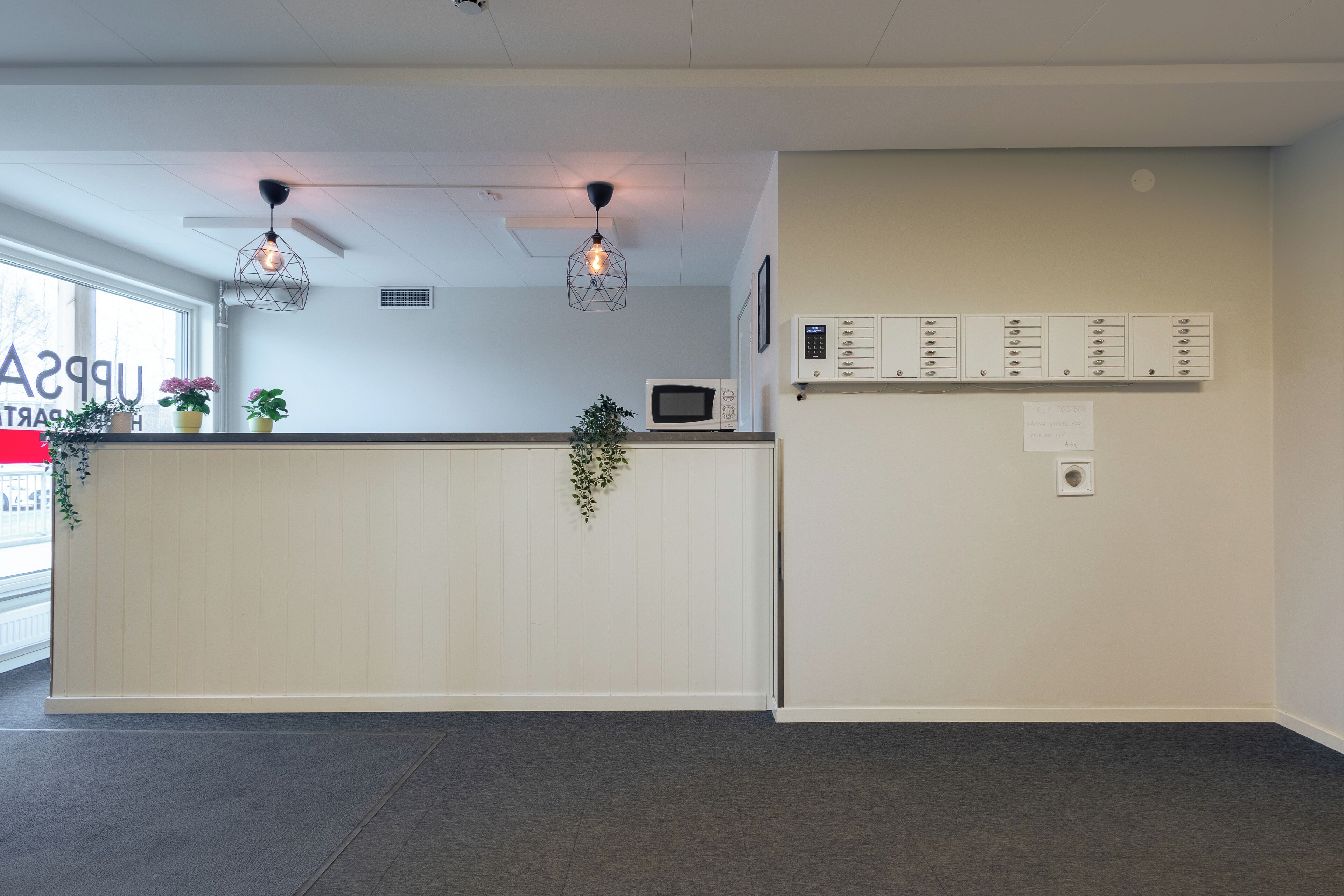 A reception area with a white counter, potted plants, a microwave, and a wall-mounted directory.
