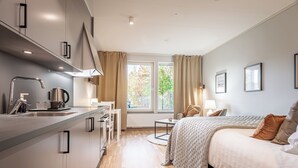 Una camera d'albergo moderna con angolo cottura, un letto vista all'esterno e un piccolo salotto.