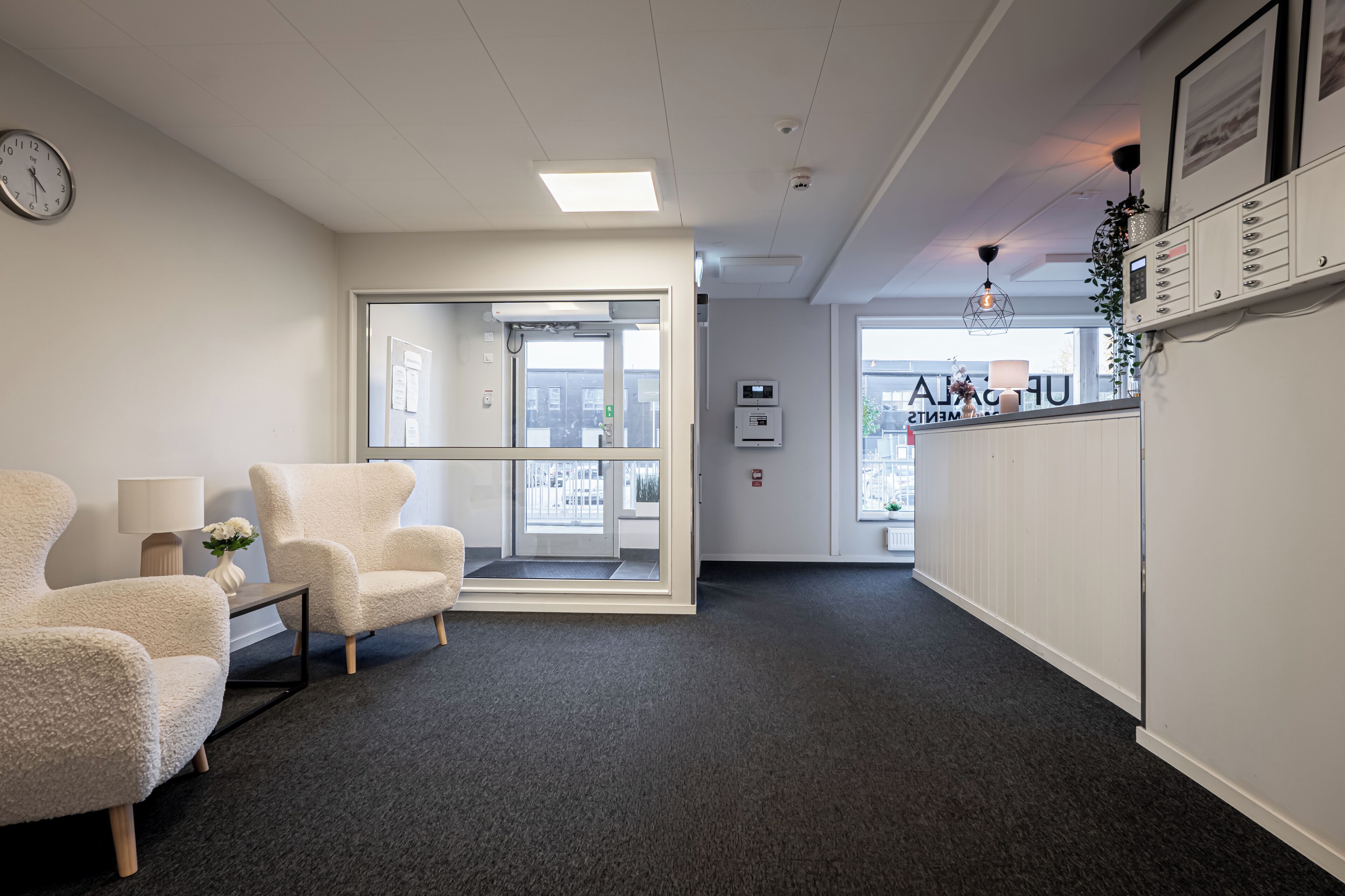 Ett receptionsområde med en receptionsdisk, stolar, en klocka och utsikt över omgivningen.