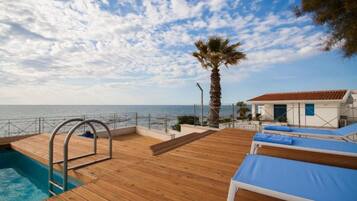 A wooden deck with a pool, lounge chairs, and a palm tree.