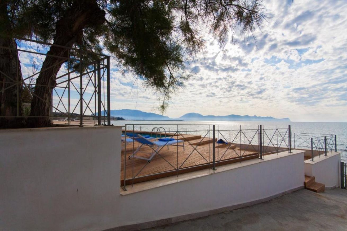 A terrace with a pool, a tree, and a view of the sea and mountains.