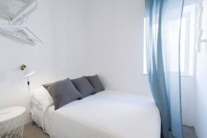 Ein Schlafzimmer mit einem Bett, einem Nachttisch, einer Lampe und einem Fenster mit Vorhängen.