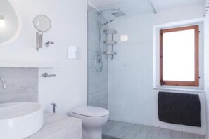 Un baño con lavamanos redondo, inodoro y ducha.