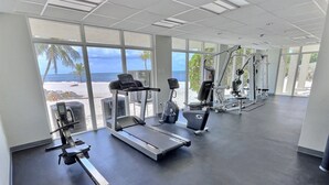 A gym with cardio machines, weight training equipment, and large windows offering a view of the beach.