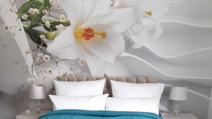 Ein Schlafzimmer mit einem Bett, weißen Kissen, einer türkisblauen Decke und einem Nachttisch mit Lampe.