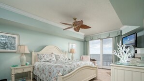 Une chambre à coucher comprenant un lit, des tables de chevet, un ventilateur de plafond, un téléviseur et une vue sur l’extérieur.