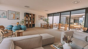 Un salon moderne avec des canapés, une table basse et une bibliothèque. De grandes fenêtres offrent une vue sur l’extérieur.