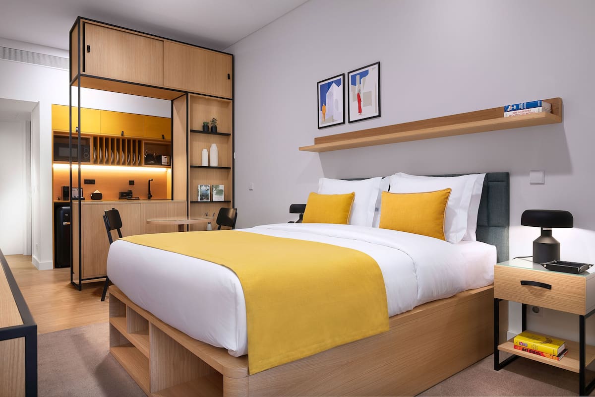 A modern hotel room with a bed, bedside table, and a built-in desk with a chair.