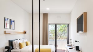 Une chambre d’hôtel moderne, équipée d’un lit, d’un bureau et d’une grande fenêtre donnant sur la verdure.
