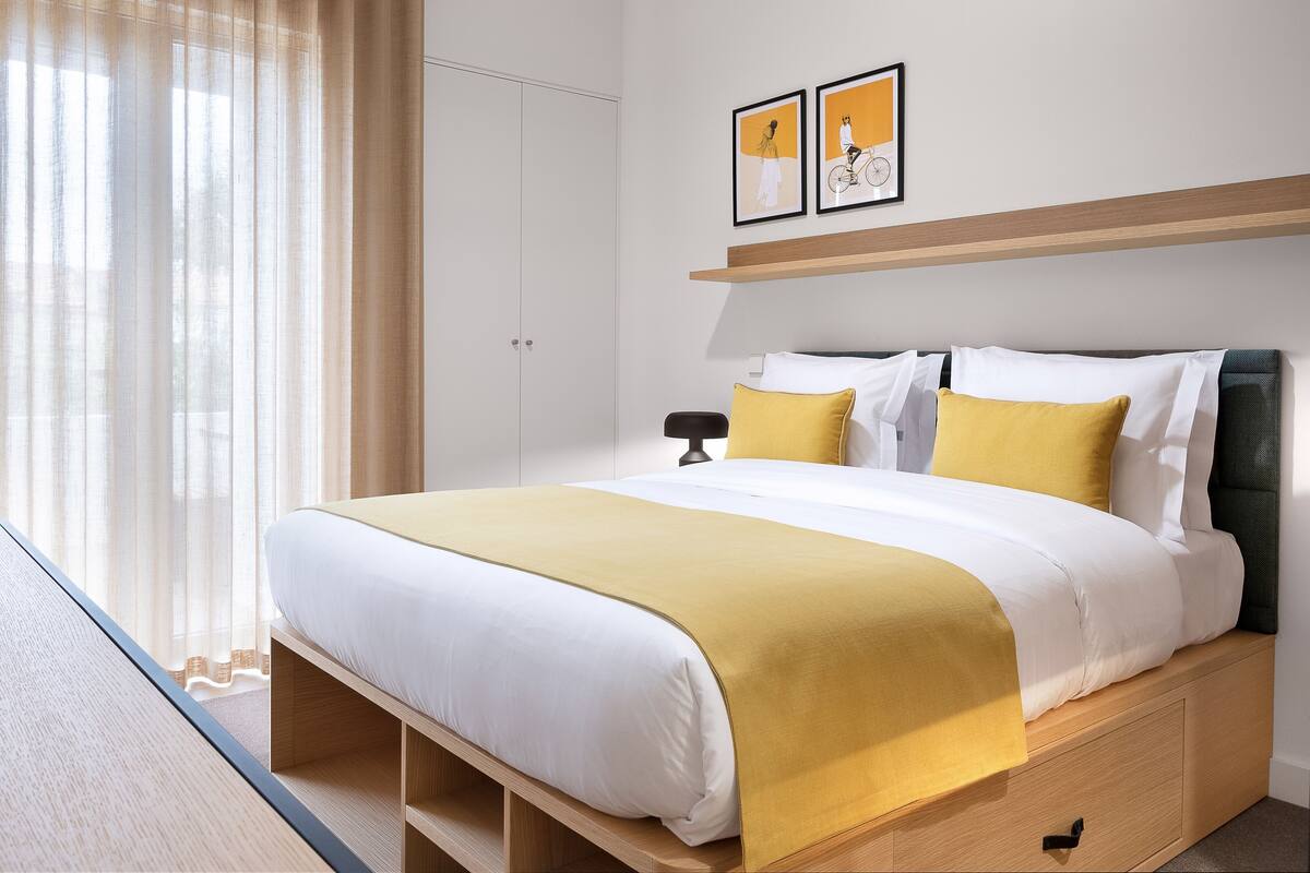 A modern hotel room with a large bed, a bedside table, a nightstand, and a wardrobe.