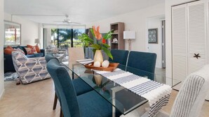 Een moderne woonkamer met een glazen eettafel, blauwe stoelen, een bank en een plafondventilator.