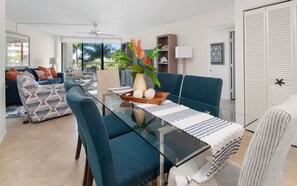 A modern living room with a glass dining table, blue chairs, and a sofa with patterned cushions.