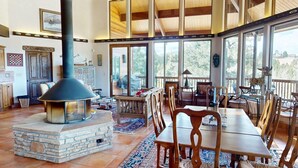 A spacious room with a stone fireplace, wooden furniture, and large windows. - Views | Pet Friendly | Folley Cabin (Angel Fire)
