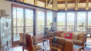 A spacious room with large windows, a wooden ceiling, and a view of the outdoors. - Views | Pet Friendly | Folley Cabin (Angel Fire)
