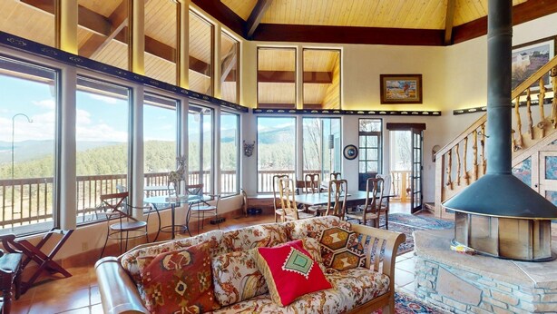 A spacious living area with large windows, a fireplace, and a dining area with outdoor views. - Views | Pet Friendly | Folley Cabin (Angel Fire)