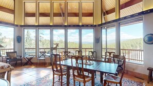 A spacious dining area with a large table and chairs, large windows with a view of the outdoors, and a wooden ceiling. - Views | Pet Friendly | Folley Cabin (Angel Fire)